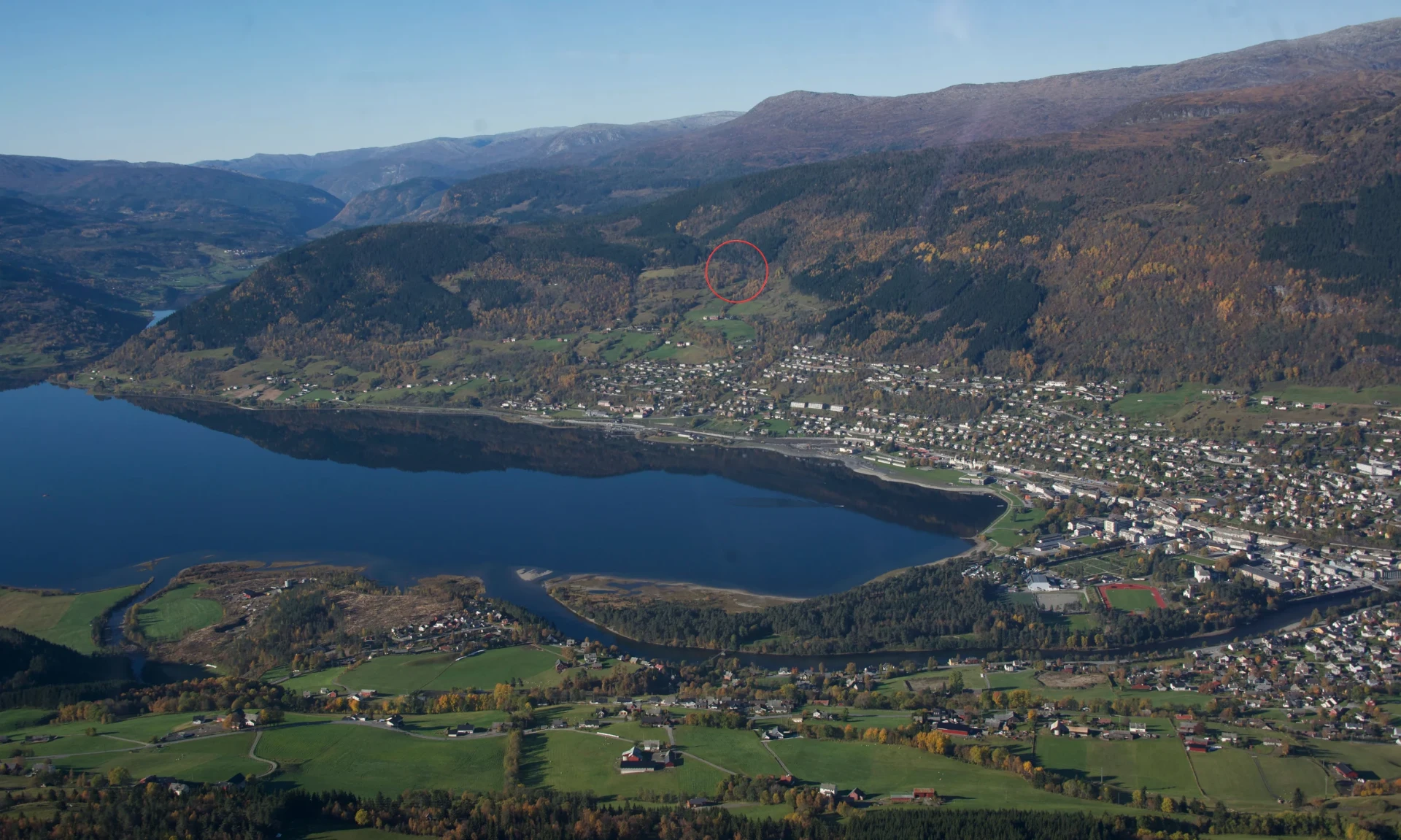 Luftfoto av Voss sentrum, Vangsvatnet og fjella omkring med hytta markert i åssida