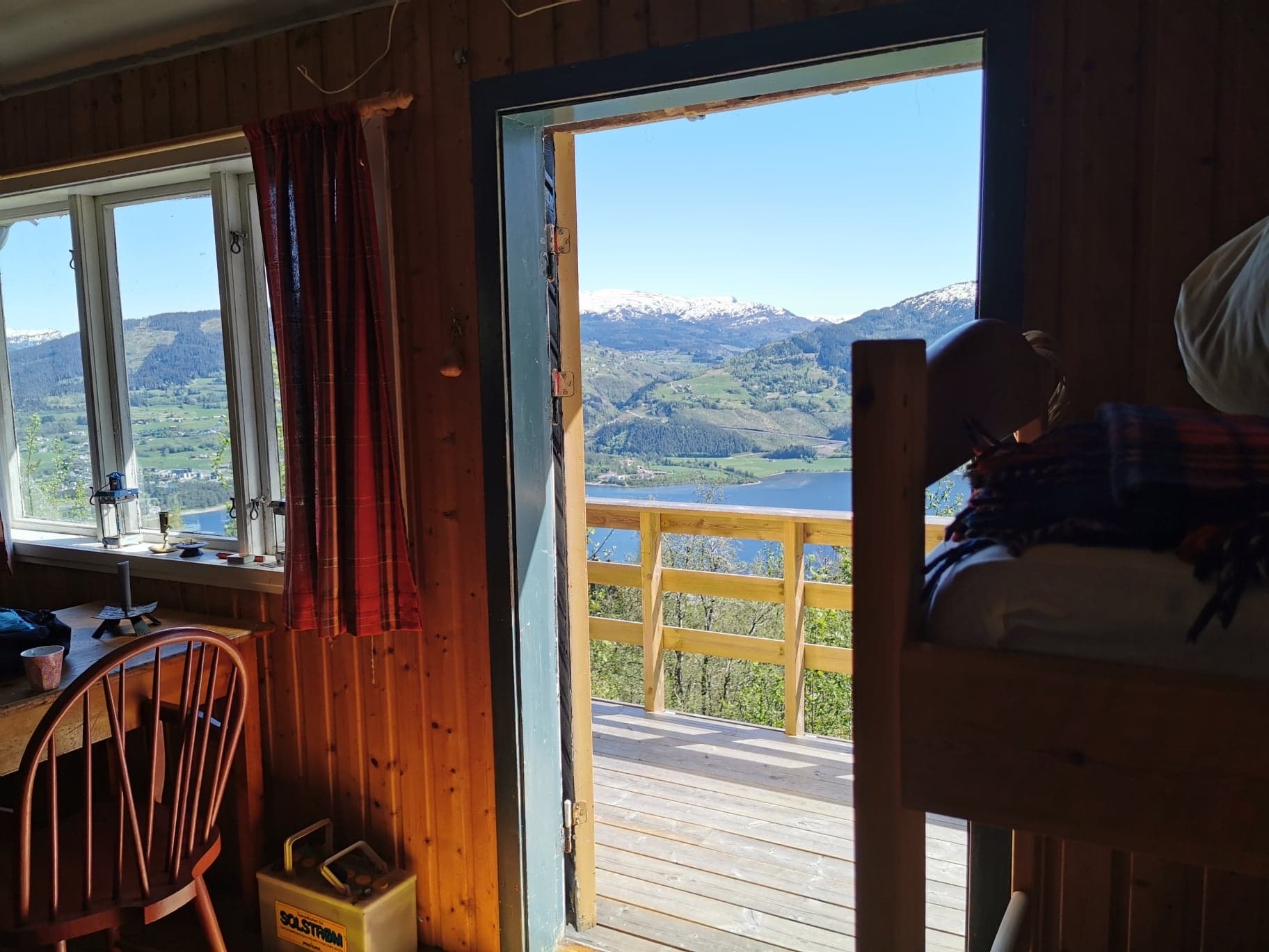 Open hyttedør med utsikt over Vossavatnet og snødekte fjell, køyeseng i forgrunnen